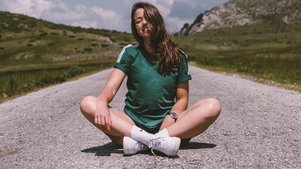 A girl sits on a road in the middle of nowhere, smiling while enjoying the warmth of the sun