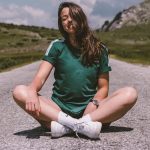 A girl sits on a road in the middle of nowhere, smiling while enjoying the warmth of the sun