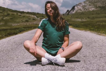A girl sits on a road in the middle of nowhere, smiling while enjoying the warmth of the sun