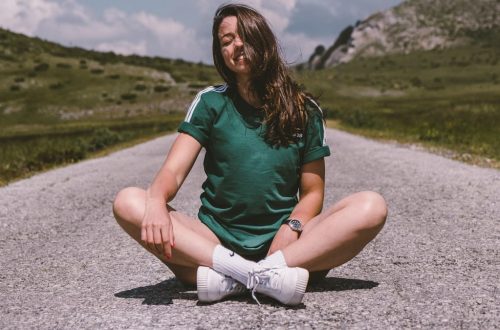 A girl sits on a road in the middle of nowhere, smiling while enjoying the warmth of the sun