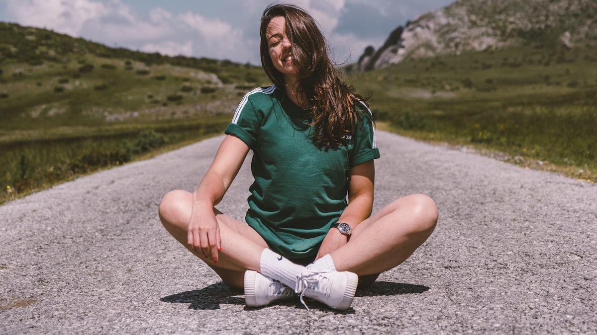 A girl sits on a road in the middle of nowhere, smiling while enjoying the warmth of the sun